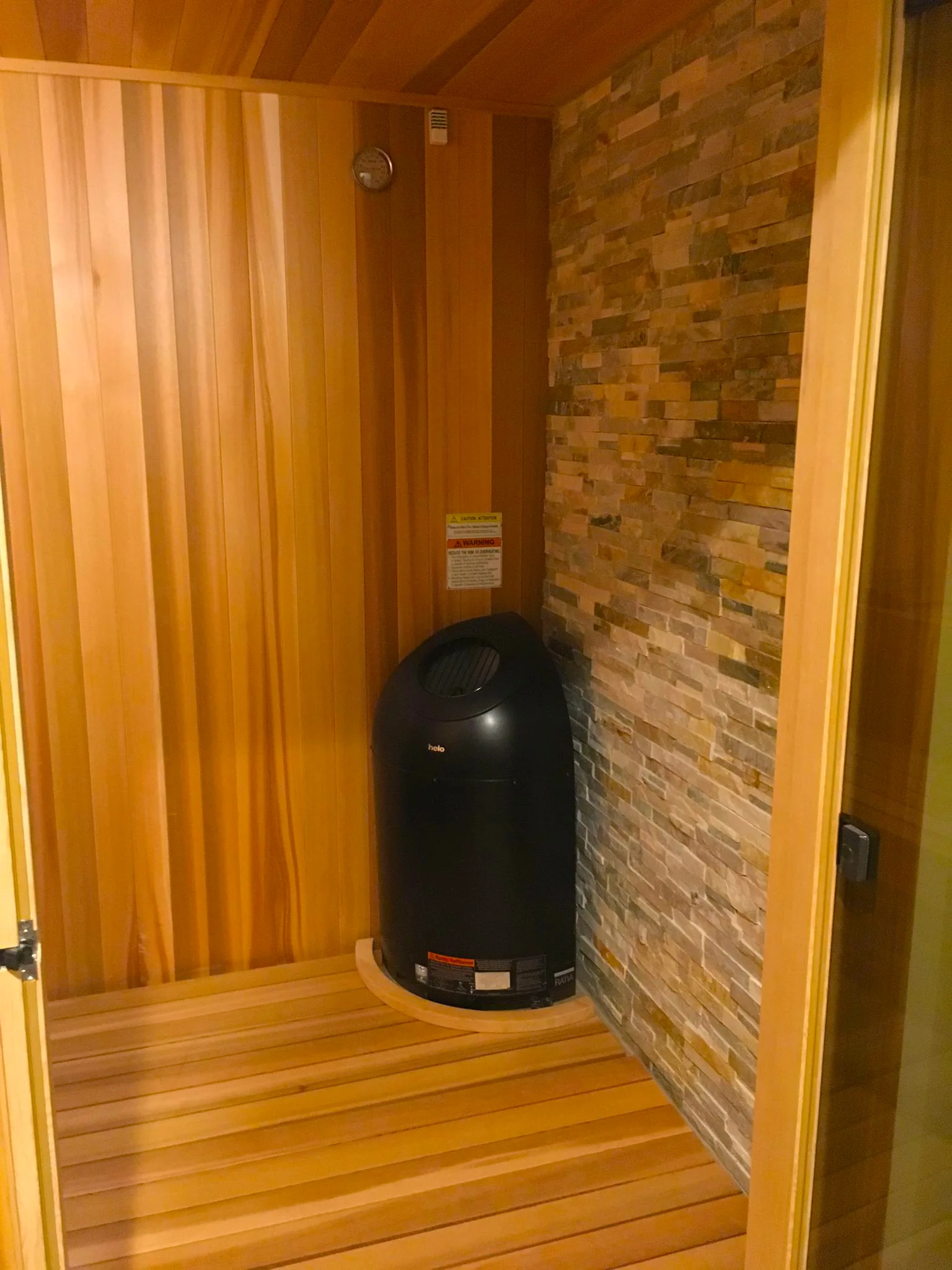 Retreat: A commercial retreat with a stone feature wall, Western red cedar walls and ceiling, an all-glass door, and a Pikkutonttu heater.